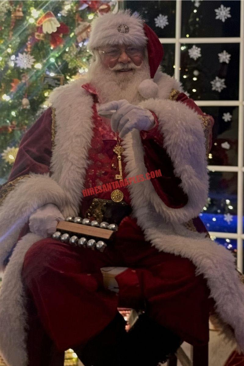 Santa home visit in Naples, FL: Santa seated with sleigh bells and a gold key beside a night window.